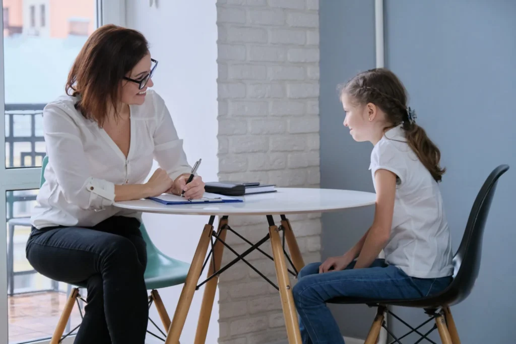 adult woman sitting at a table with a young girl talking.