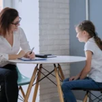 adult woman sitting at a table with a young girl talking.