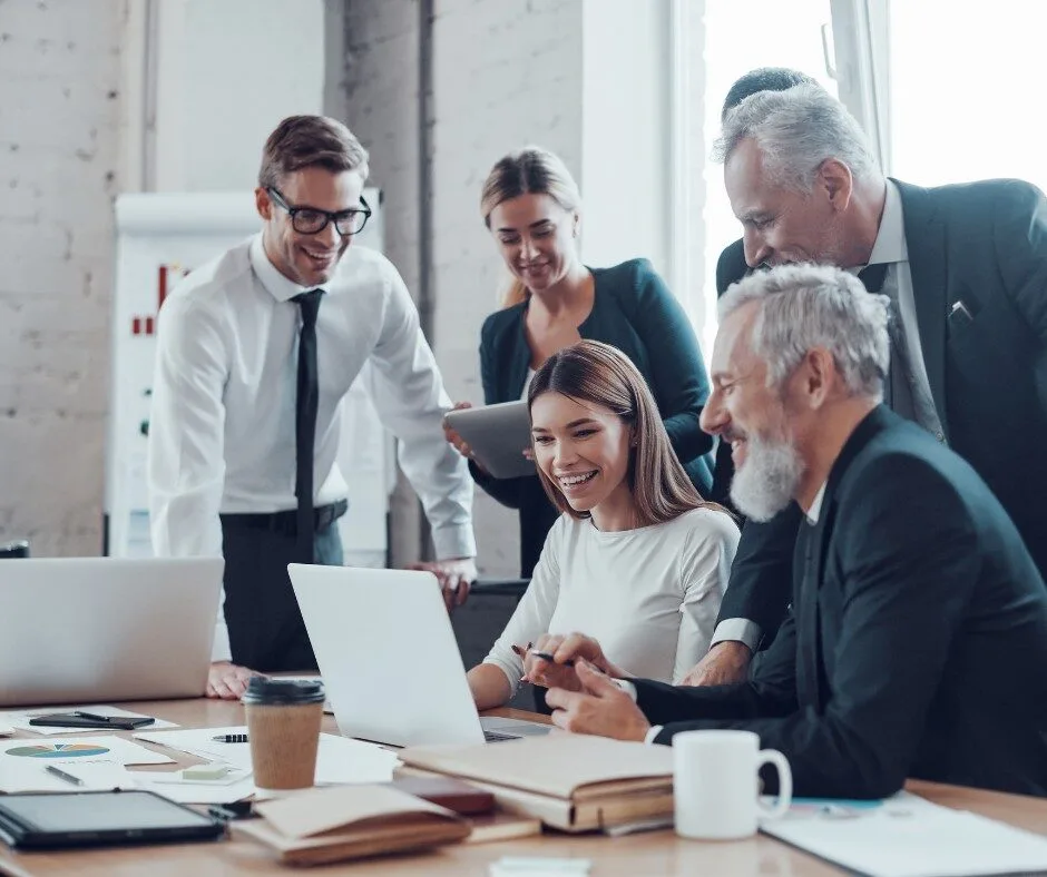 group sitting and standing around a table looking at a laptop collaborating